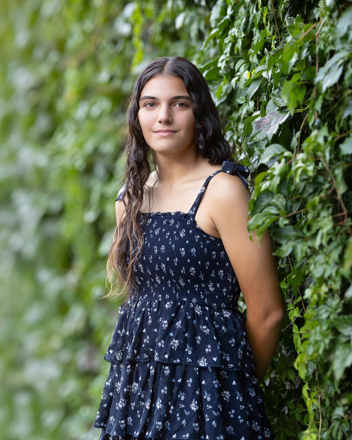 High school senior girl with long dark hair leaning against a green ivy wall in Lowell Massachusetts